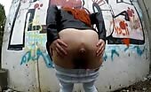 Red-haired girl pooping outside by a wall