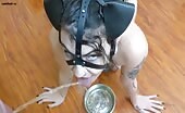 Woman in leather headgear drinks piss from metal bowl